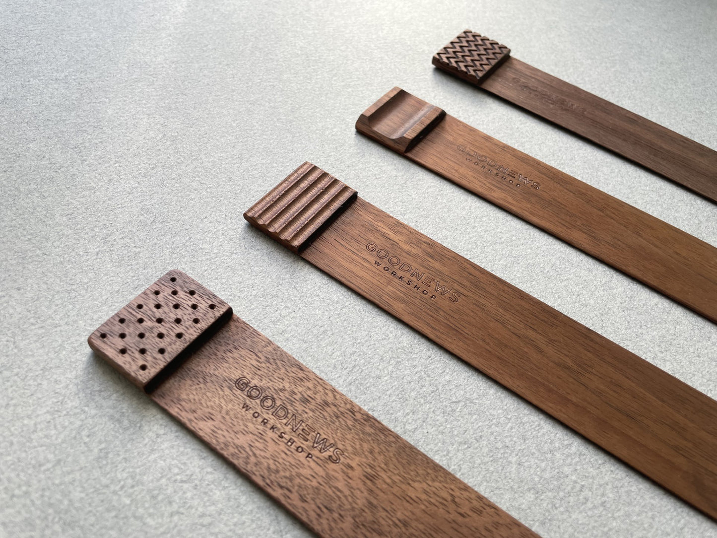 Four walnut Edge Bookmarks with the upper edge step shown different engraved textures on a gray background. Perforated, Flutes, Groove and Zigzag. Detail angled view of engraved designs.