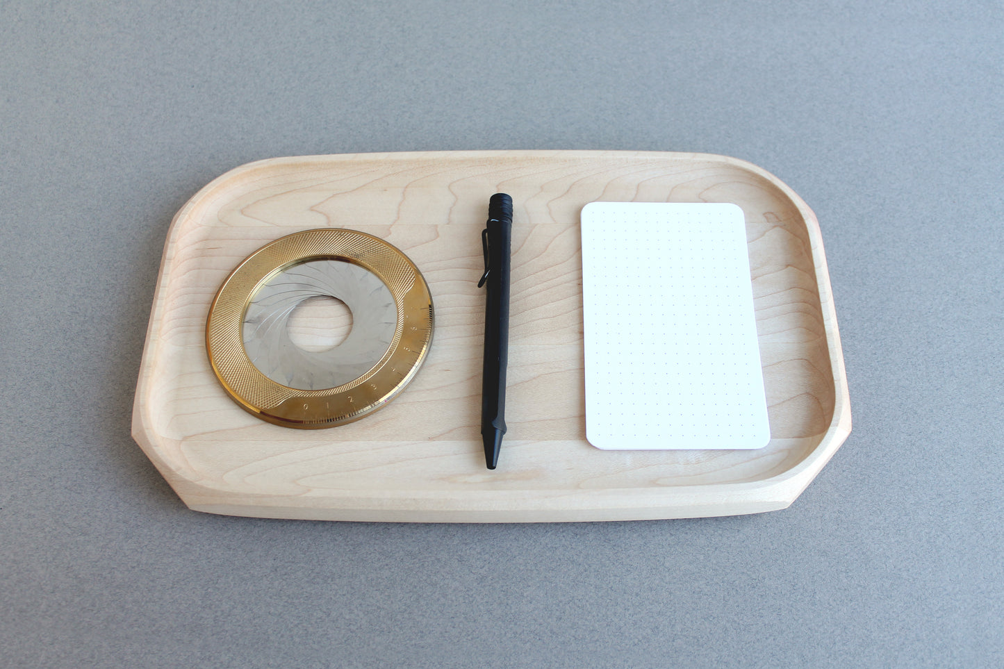 Genesis Tray in Maple wood on gray background. Top view with circle template, pen and notecard on it.