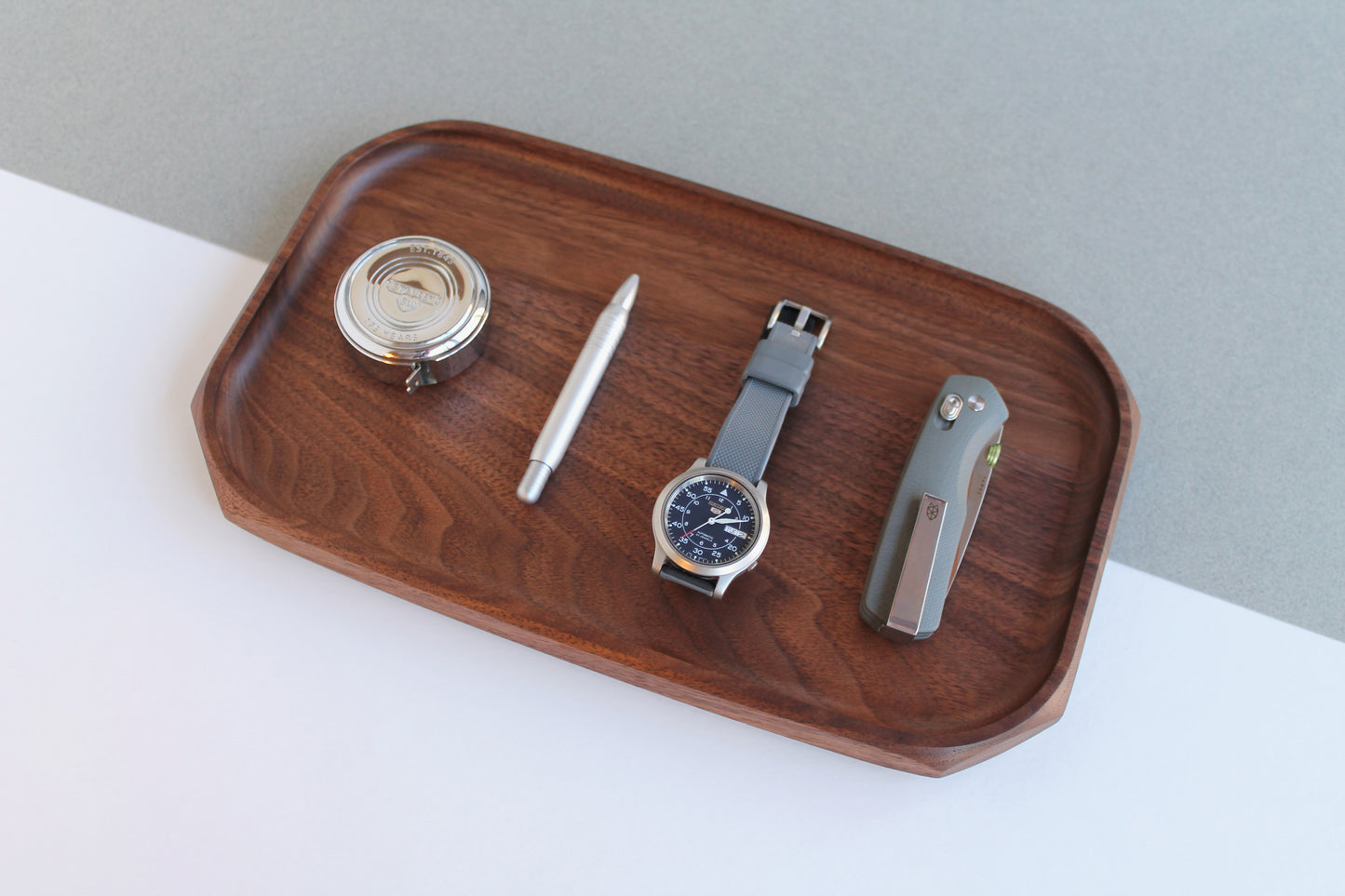 Genesis Tray in Walnut wood on gray and white angled background. Angled view with pocket knife, watch, pen and tape measure on tray.