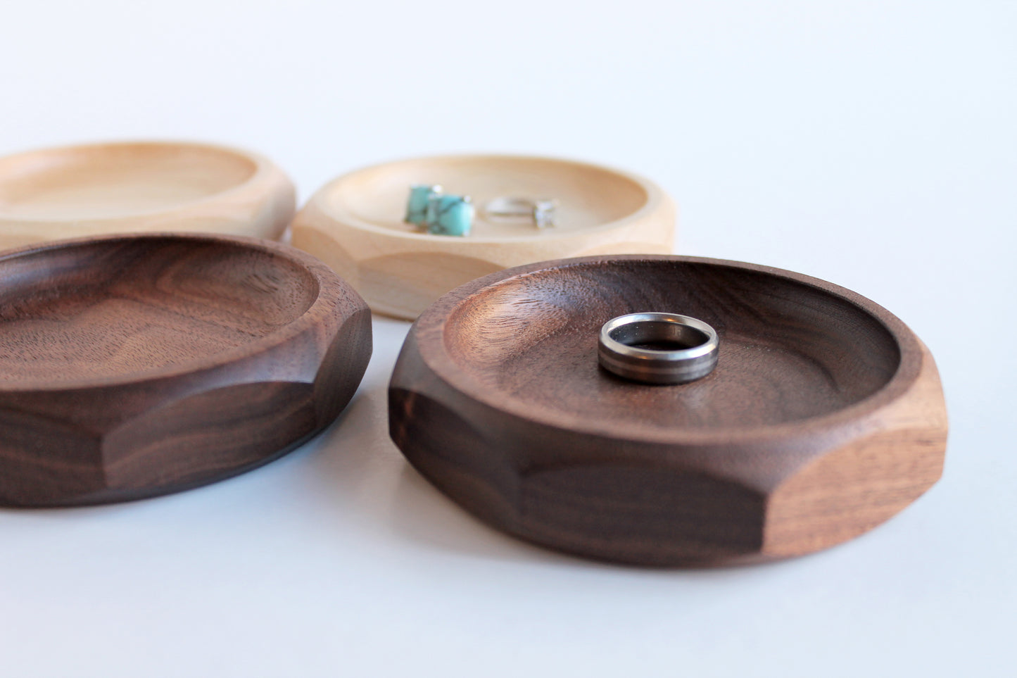 Genesis Dish detail view of two maple and two walnut dishes with rings and earrings in them.