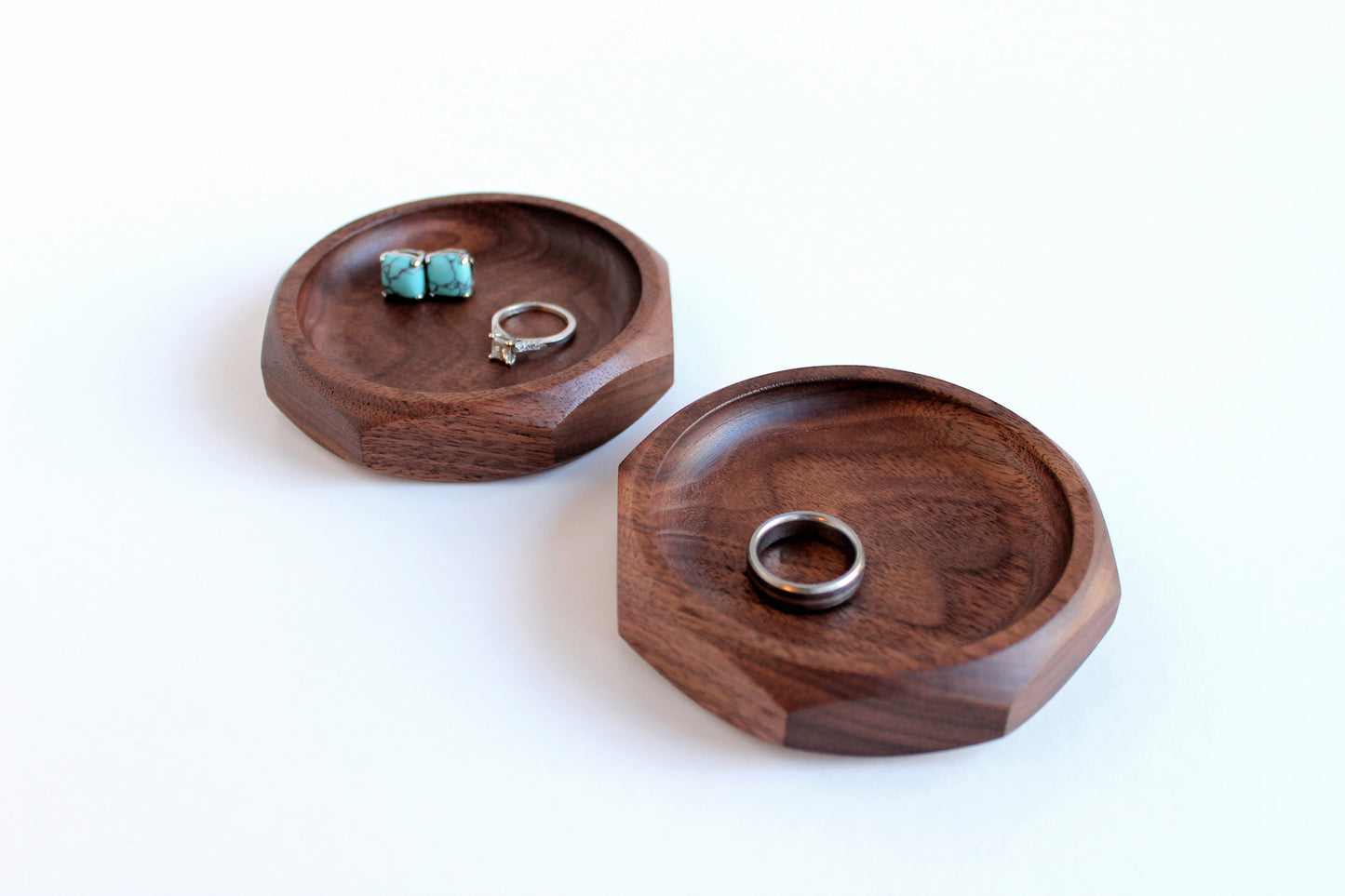 Two Genesis Dishes in walnut on white background with rings and earrings in them.