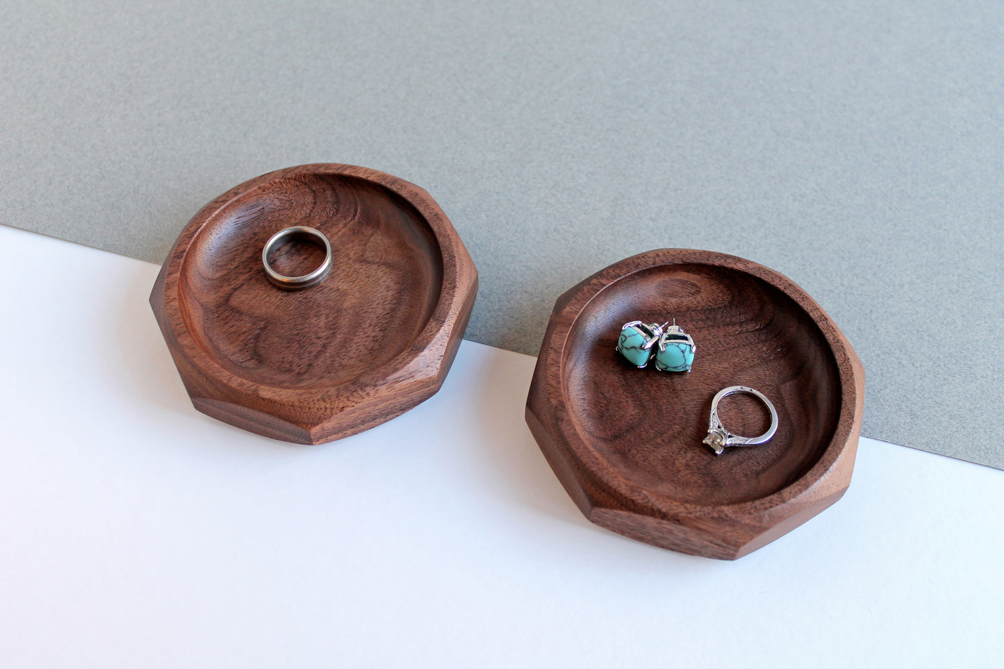 Two Genesis Dishes in walnut on gray and white angled background with rings and earrings in them.