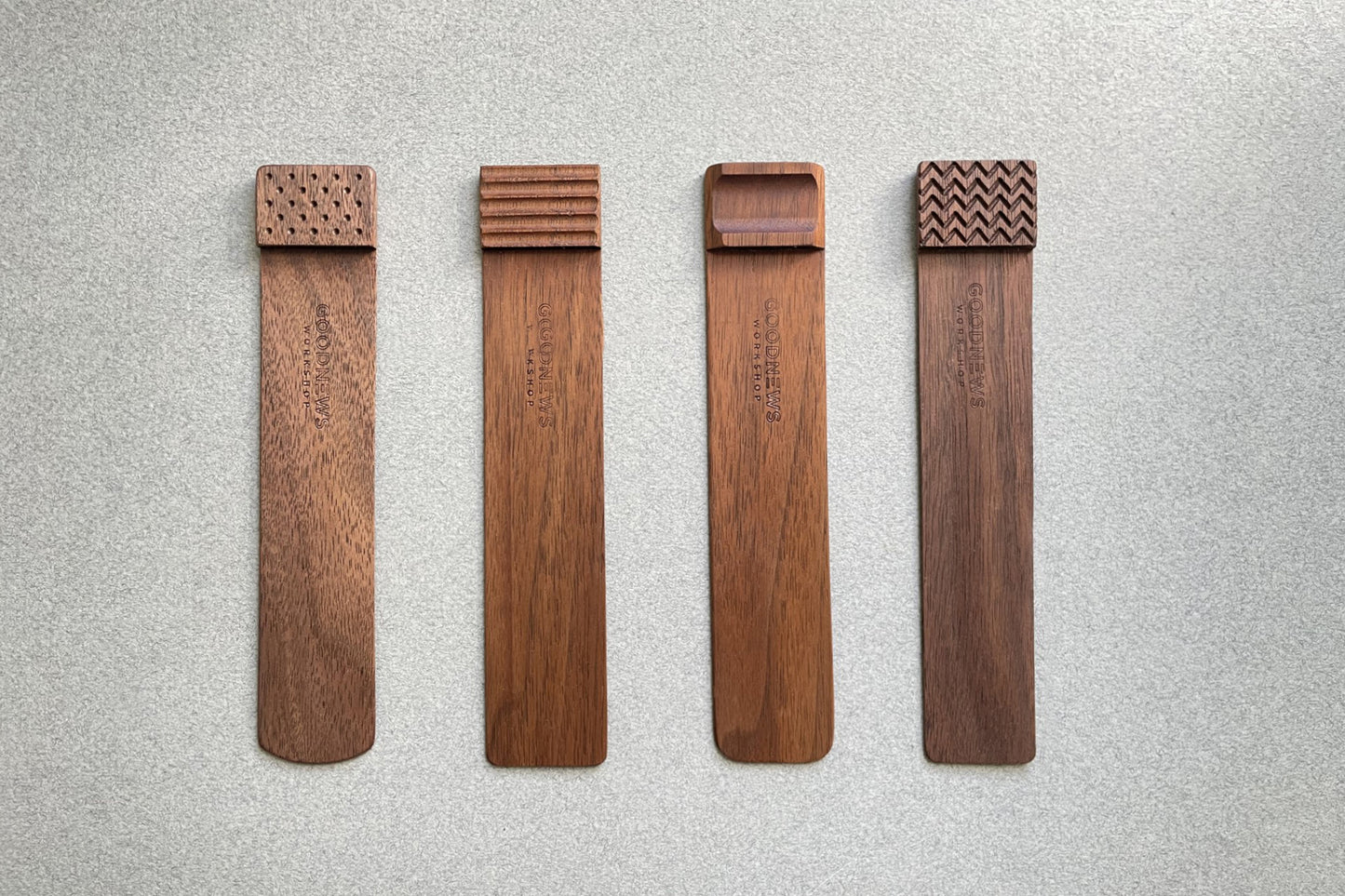 Four walnut Edge Bookmarks with the upper edge step shown different engraved textures on a gray background. Perforated, Flutes, Groove and Zigzag