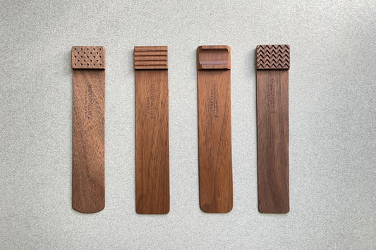 Four walnut Edge Bookmarks with the upper edge step shown different engraved textures on a gray background. Perforated, Flutes, Groove and Zigzag